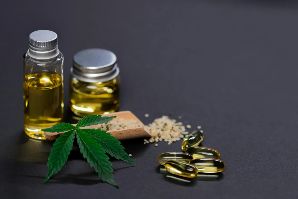 CBD oil bottles, hemp capsules, and a cannabis leaf displayed with hemp seeds on a dark surface